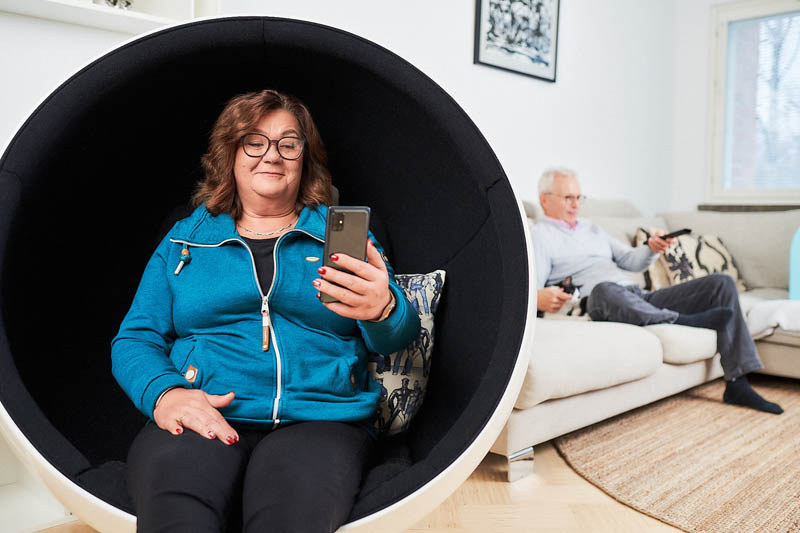 Asiakas käyttää älypuhelinta kotonaan nojatuolissa istuen.